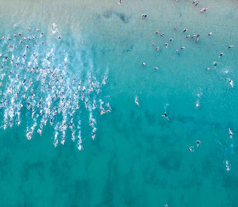 A photo of a bright blue ocean, with a huge number of triathletes swimming in it