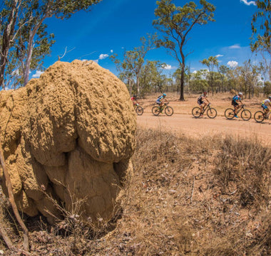 A group of riders racing in the outback, with blue skies and red dirt