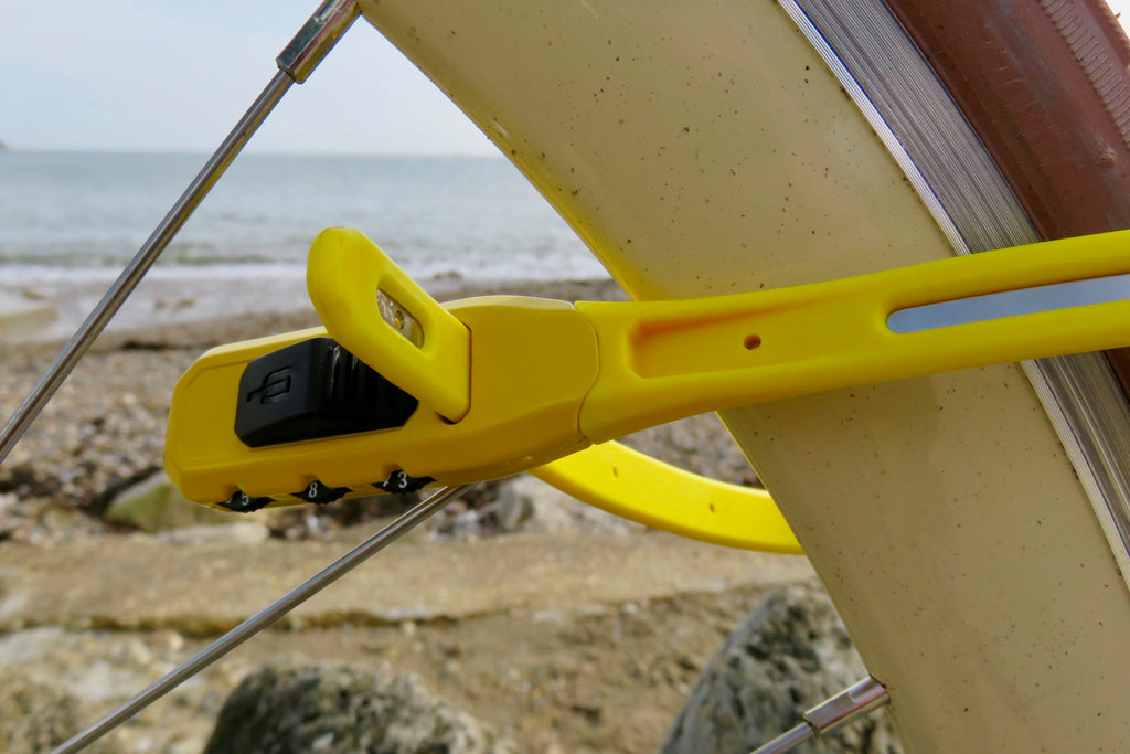 A close up photo of the Hiplok Z Lok combo lock attacked to a vintage cruiser bike's wheel, with a beach in the background